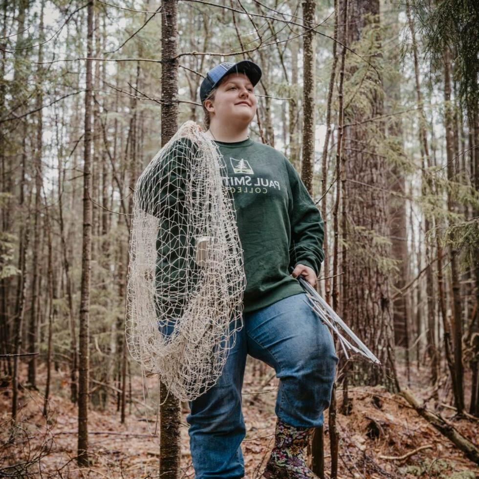 Student holding a net walking through the woods